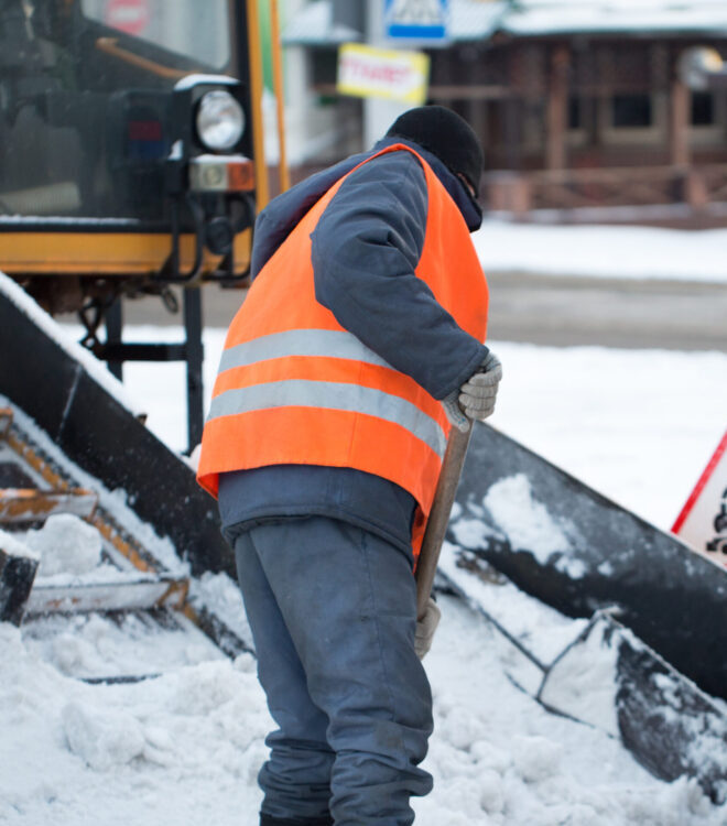 Tractor cleaning the road from the snow. Excavator cleans the streets of large amounts of snow in city. Workers sweep snow from road in winter, Cleaning road from snow storm.