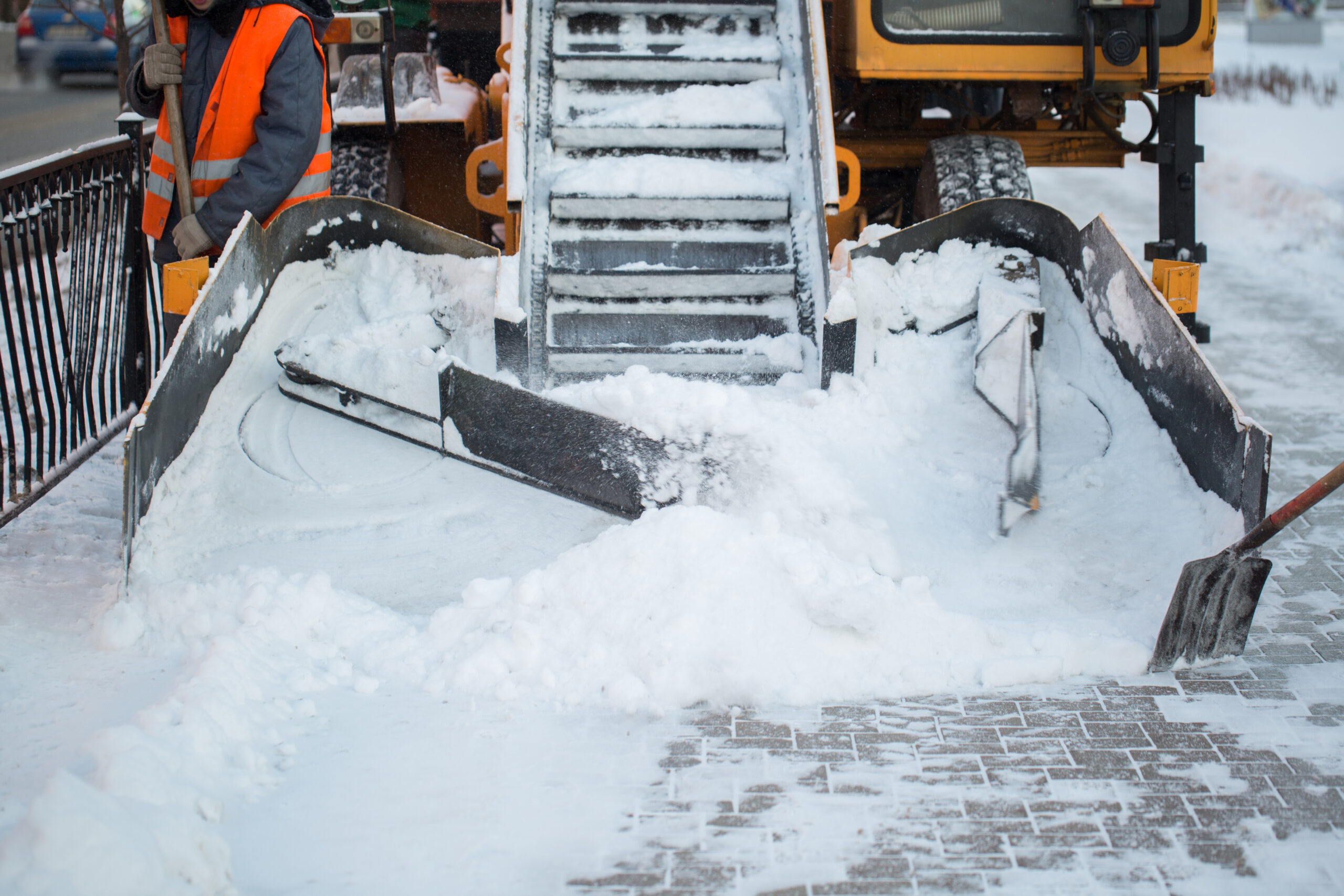 Tractor cleaning the road from the snow. Excavator cleans the streets of large amounts of snow in city. Workers sweep snow from road in winter, Cleaning road from snow storm.